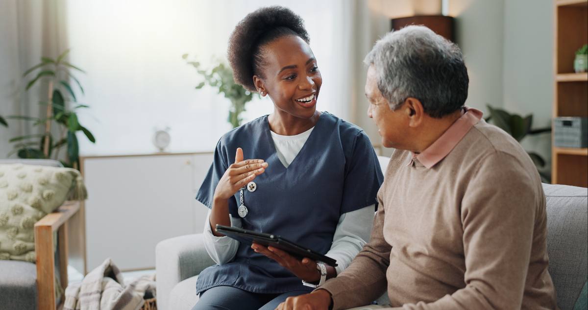 Healthcare worker in navy scrubs discussing tablet with senior male patient in home setting