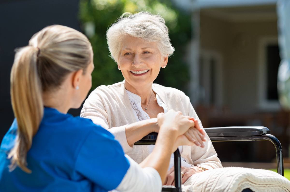 Healthcare worker in blue uniform assisting smiling senior woman outdoors